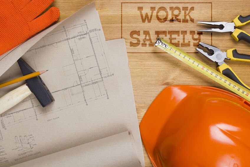 ‘Work Safely’ sign surrounded by construction hats and worksite blueprints