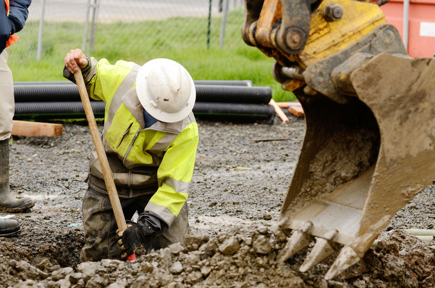 Worker using a small, tracked excavator to dig a hole to fix a water leak at a large commercial housing development in the muddy spring weather.